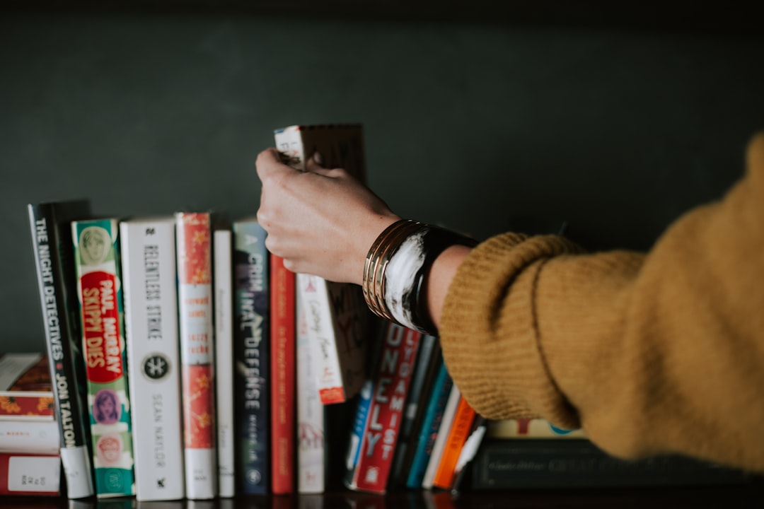 A hand in a knitted sleeve pulling one book out of a crowded shelf